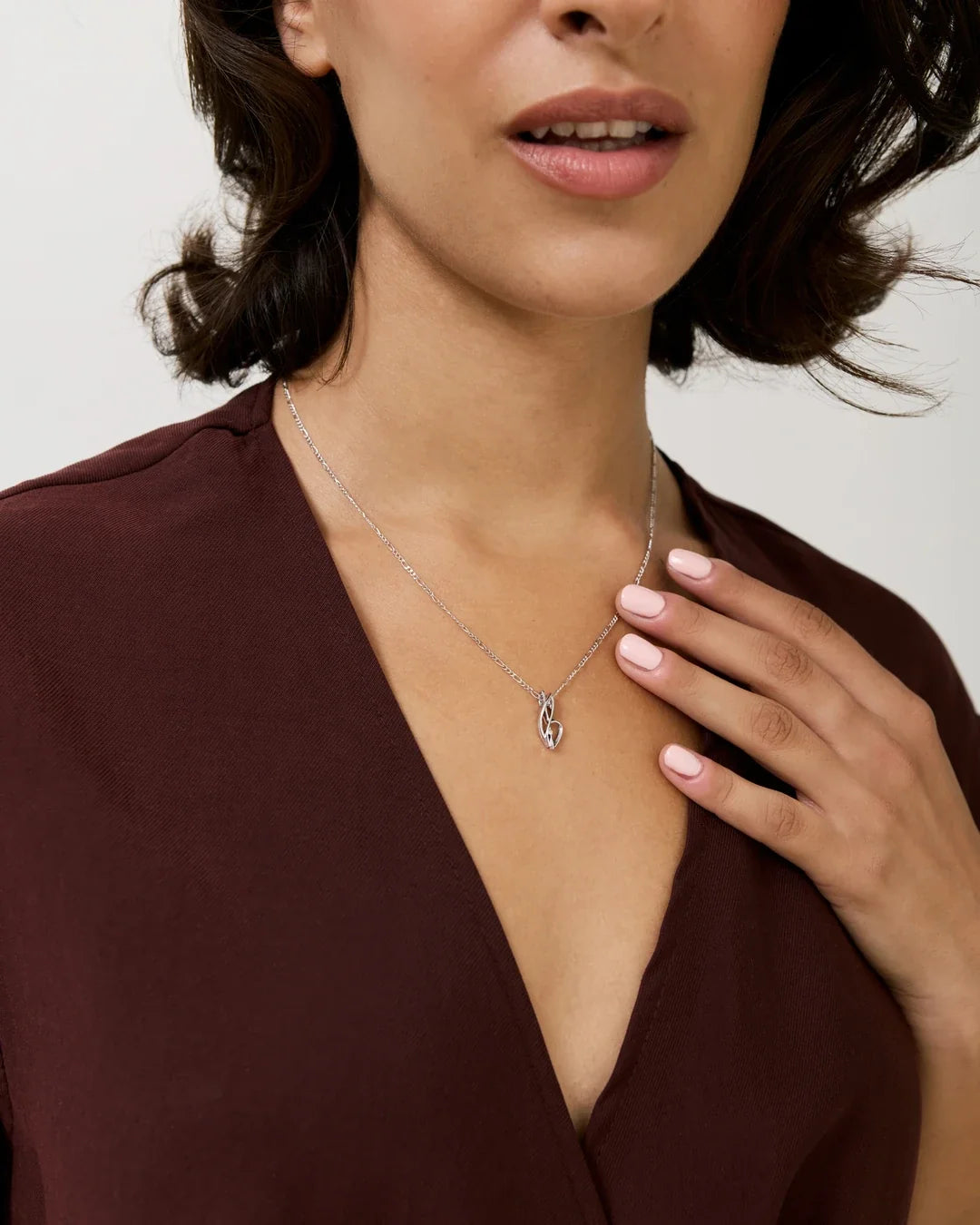 B बी Initial Necklace in a delicate silver-tone chain with a small curved letter pendant, worn over a burgundy top.