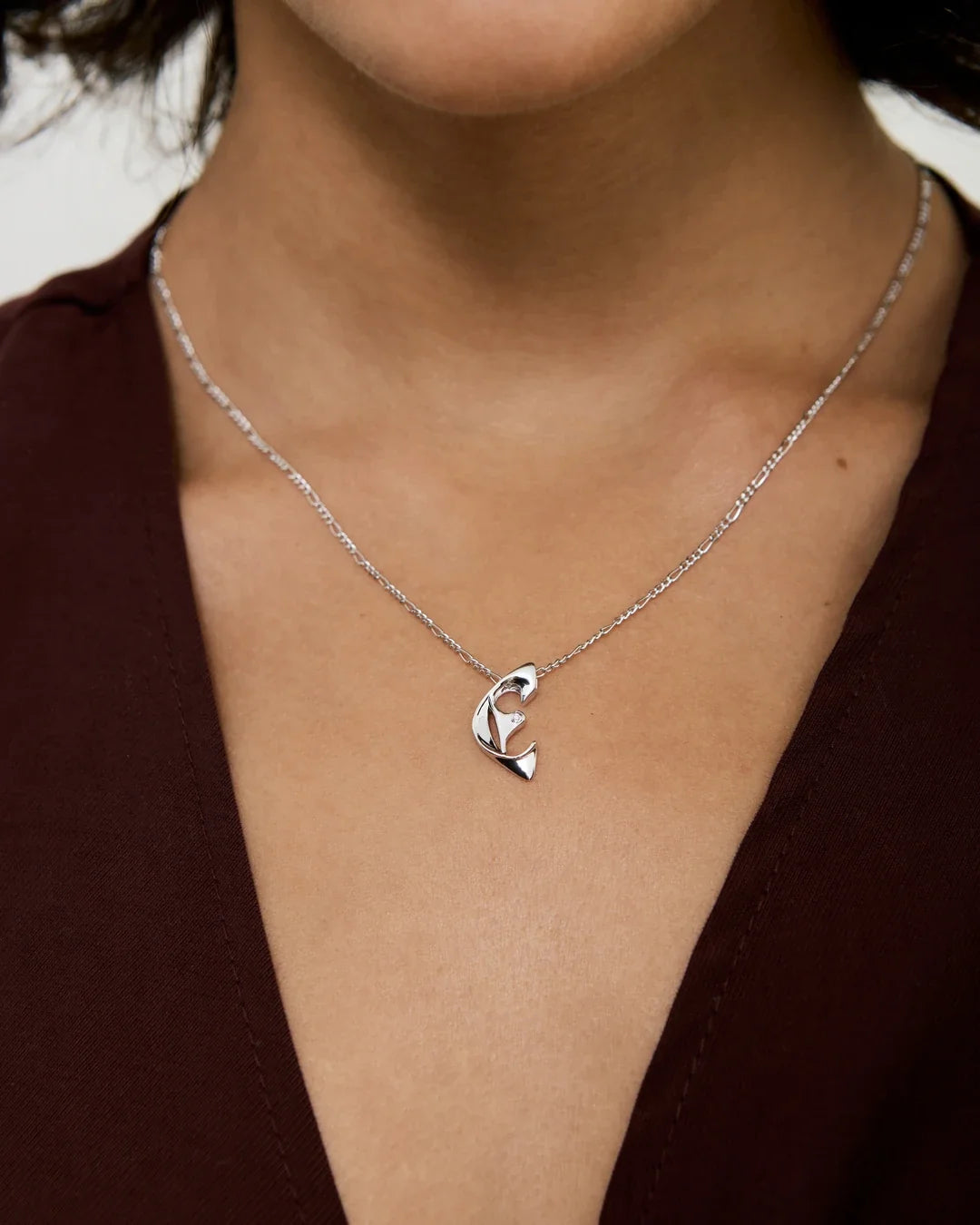 E ई Initial Necklace in polished silver, with a delicate chain and sculpted letter E pendant featuring curved cutouts.