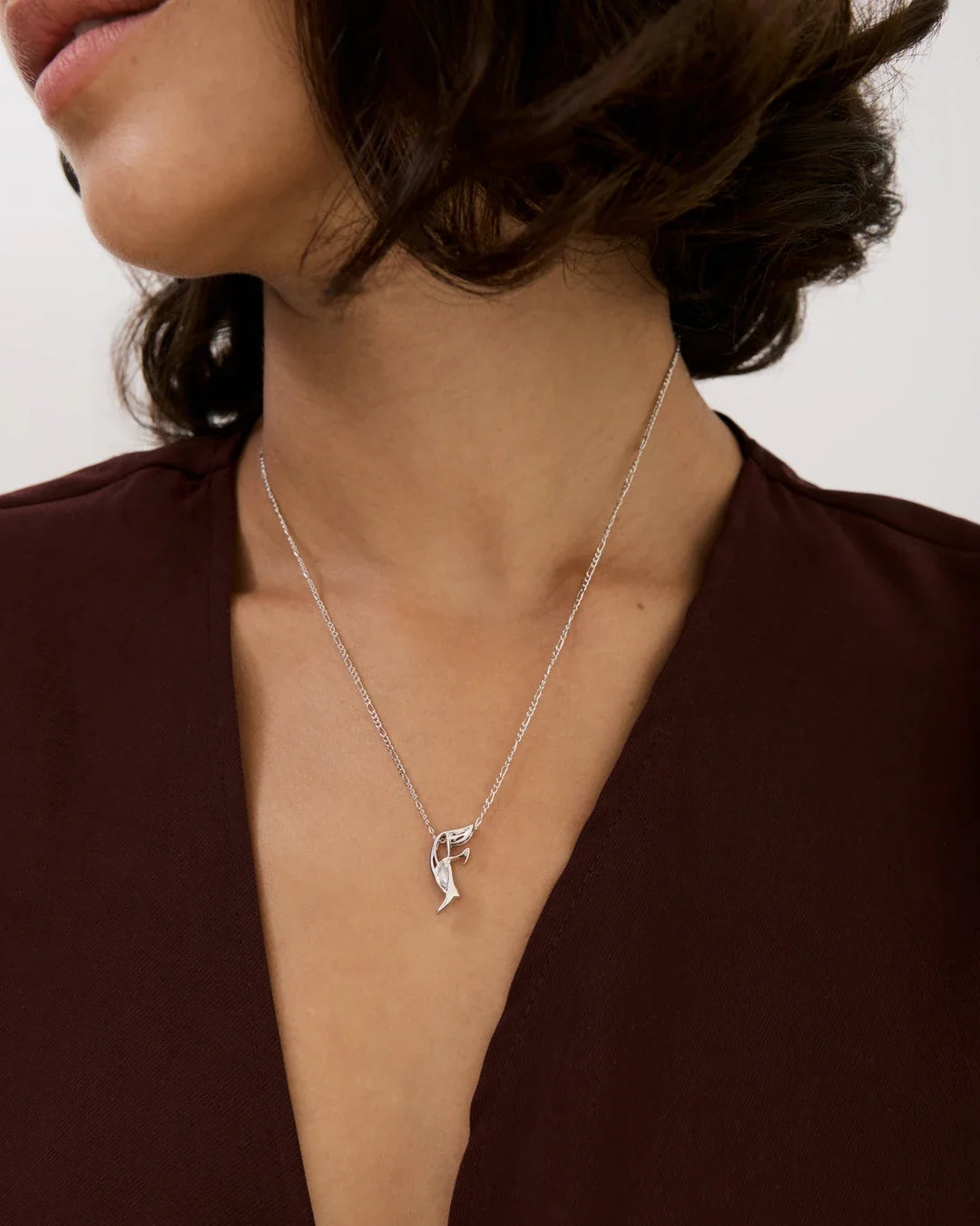 F एफ Initial Necklace in silver-tone metal, with a delicate chain and sculpted F-shaped pendant accented by a curved detail.