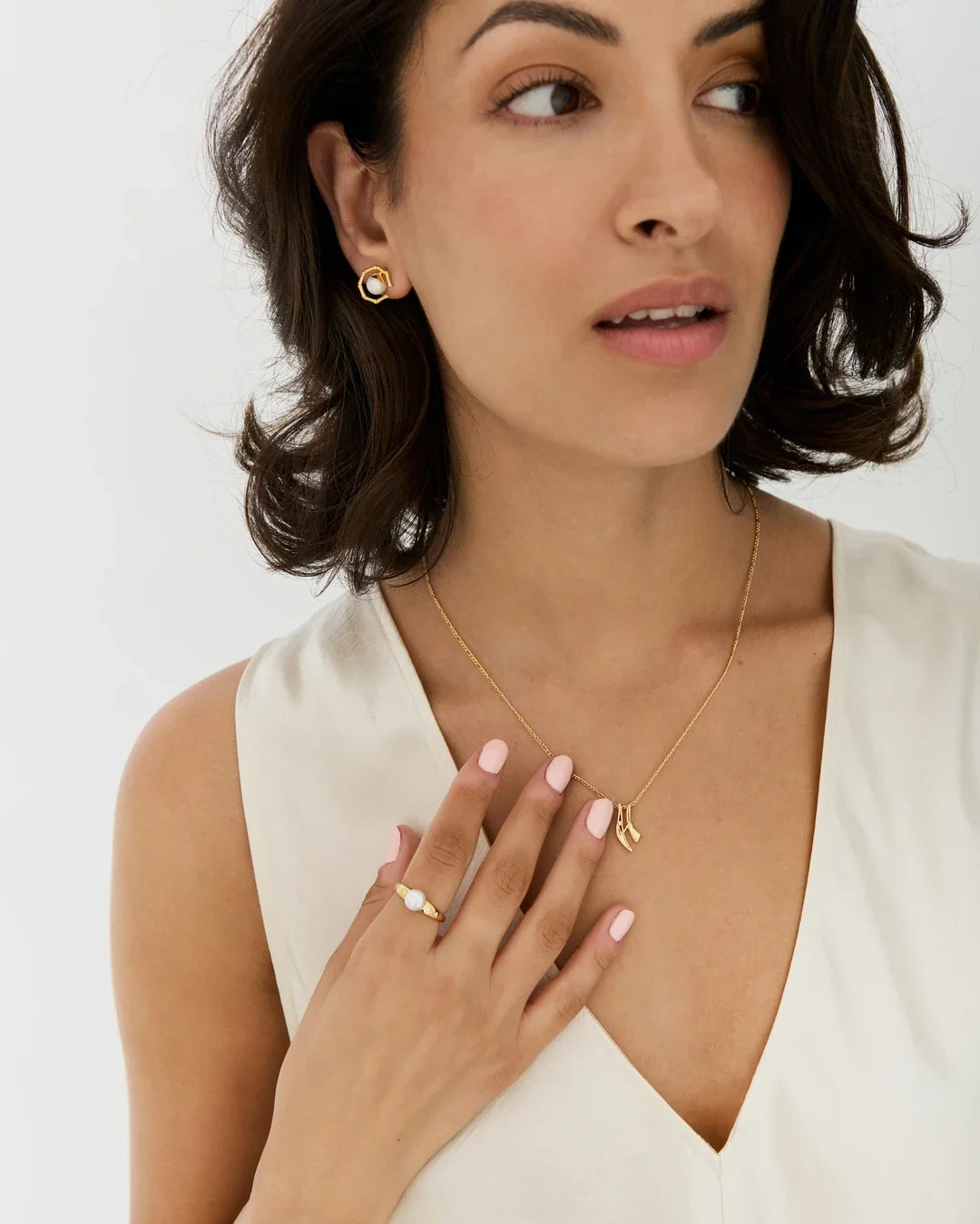 H एच Initial Necklace in a fine gold-tone chain with a small gold letter H pendant, worn over a white top.