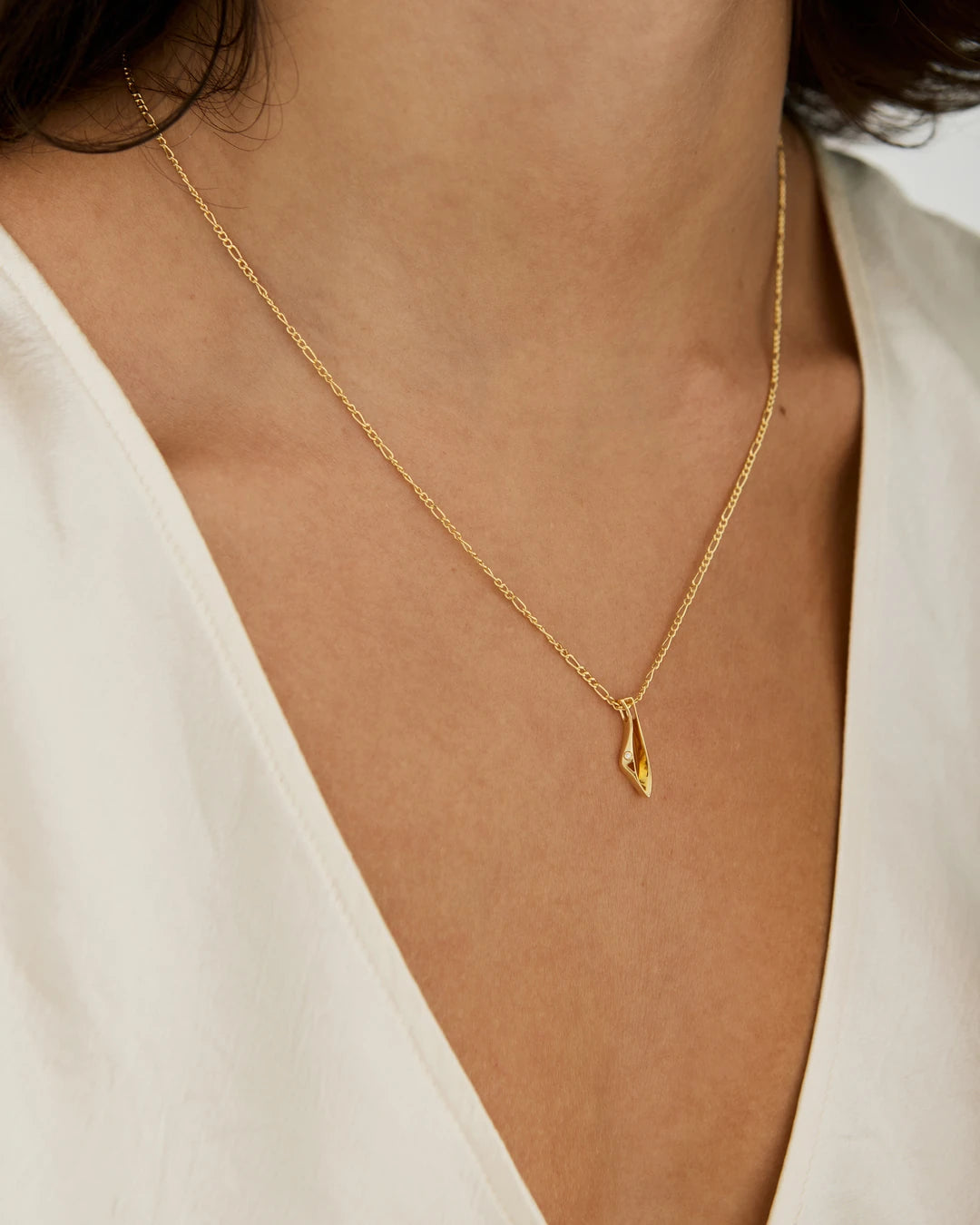 A delicate gold initial necklace with the letter 'I' pendant by NIMMISHA jewellery London, worn by a model in a white V-neck top.