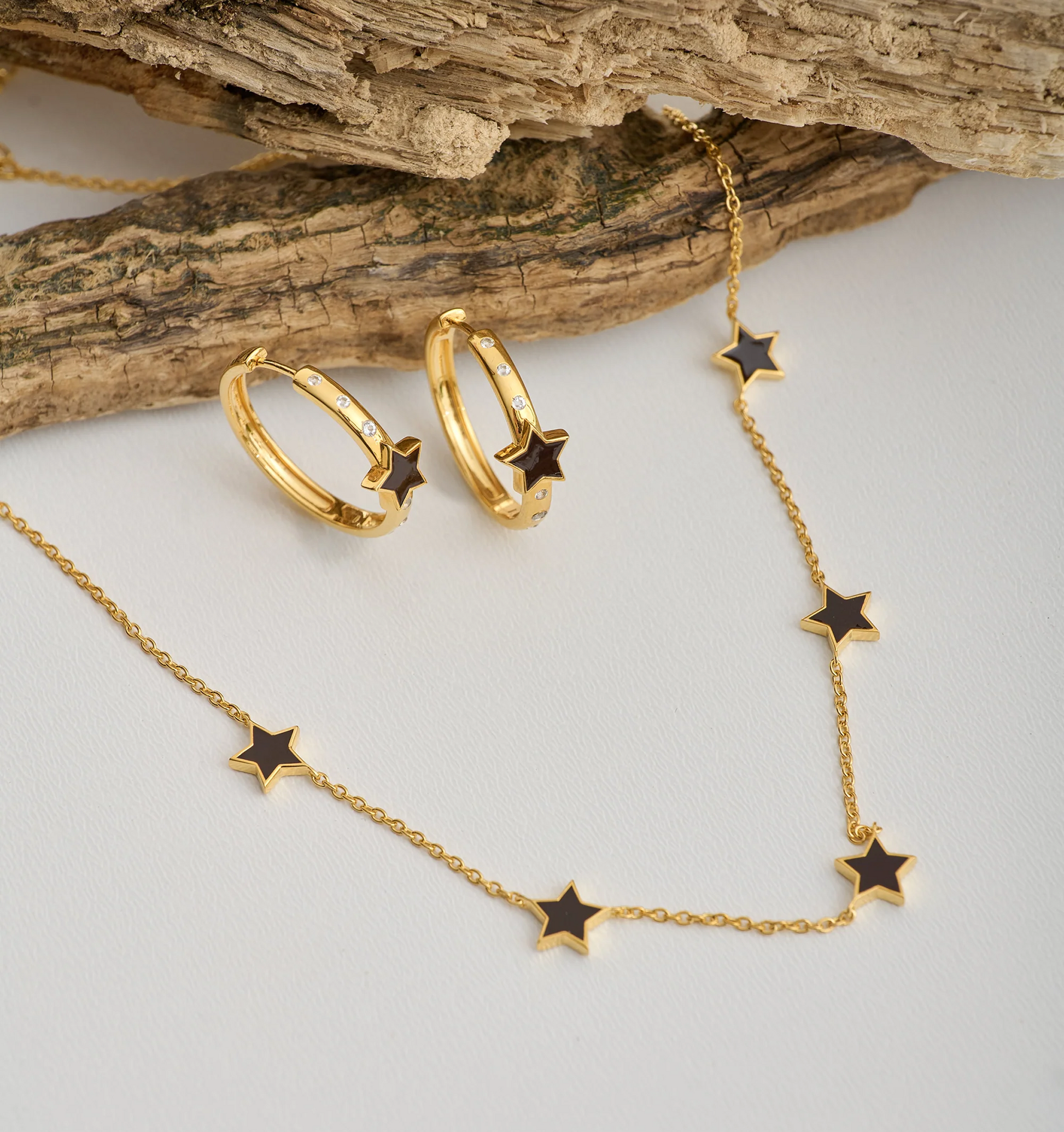 Tara Nova Hoop gold earrings with star design and matching star necklace on rustic wood background