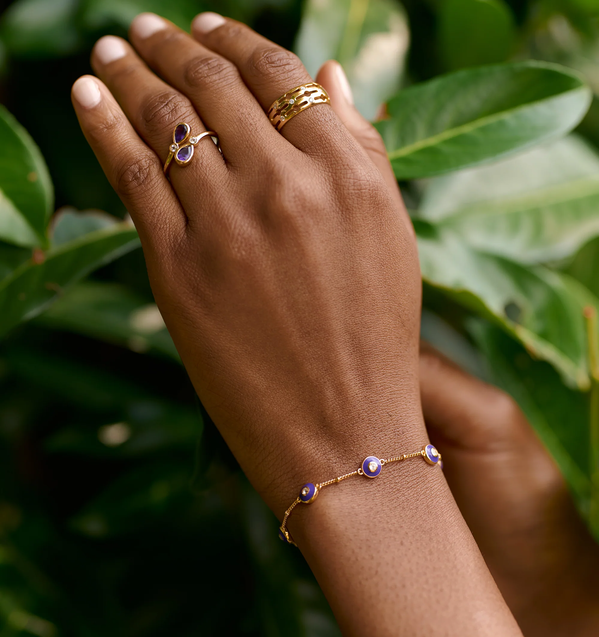 Viraah Bracelet with violet enamel and white topaz on wrist against green leaves background