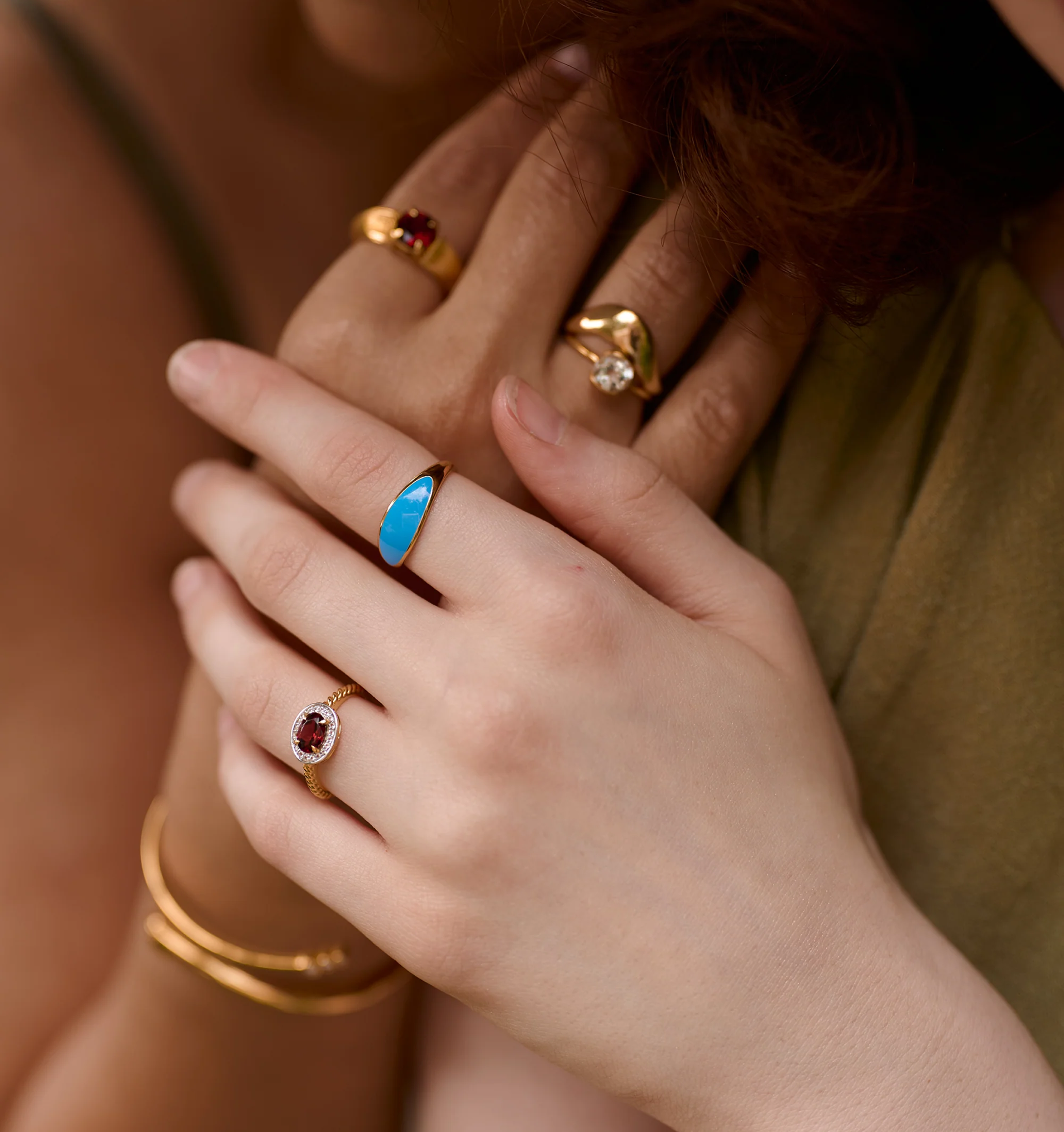 Close-up of hands wearing Neelra Ring with blue stone and gold bands inspired by water shapes