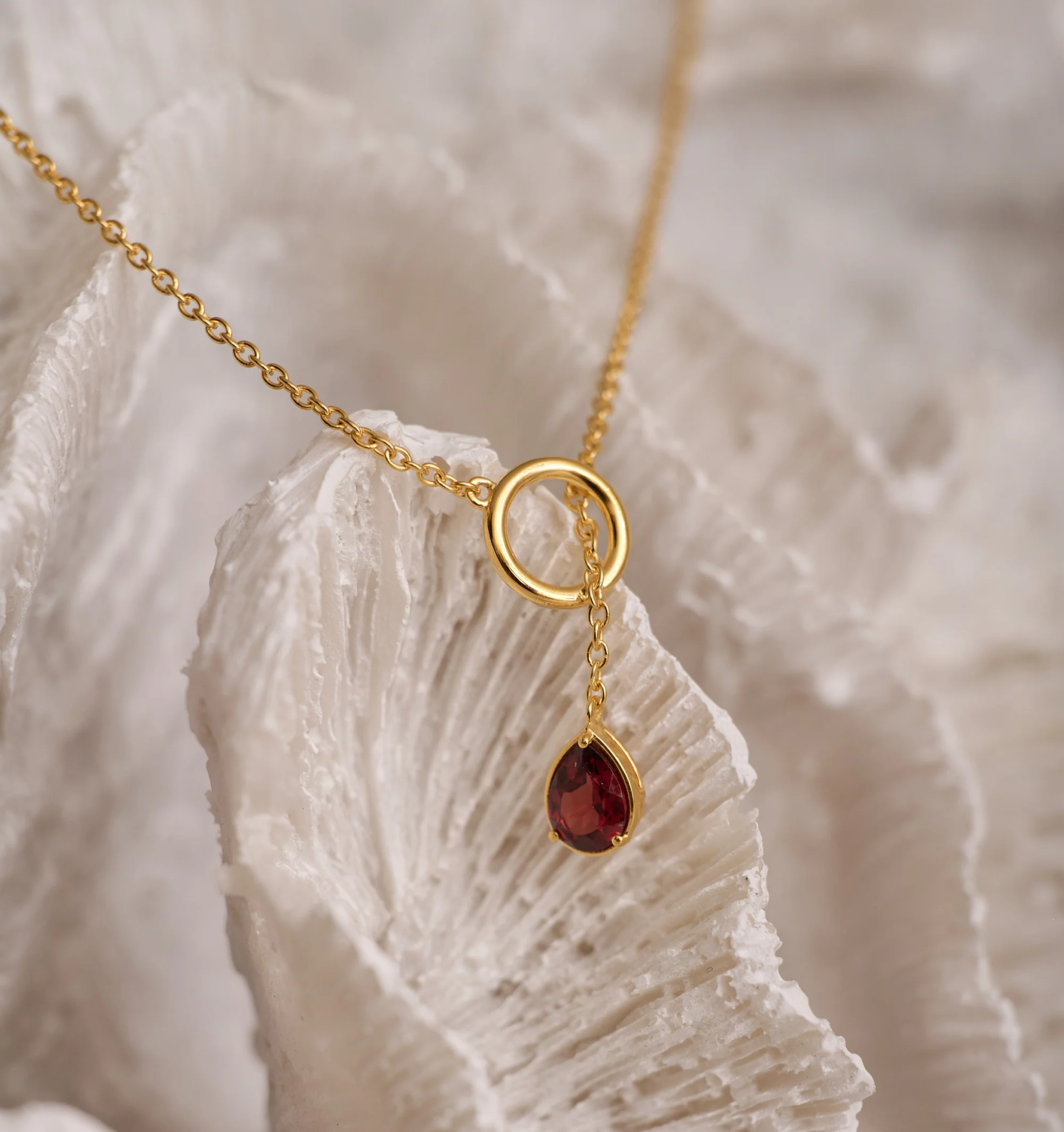 Agniti Necklace featuring a gold chain with a teardrop garnet pendant suspended from a circular gold ring