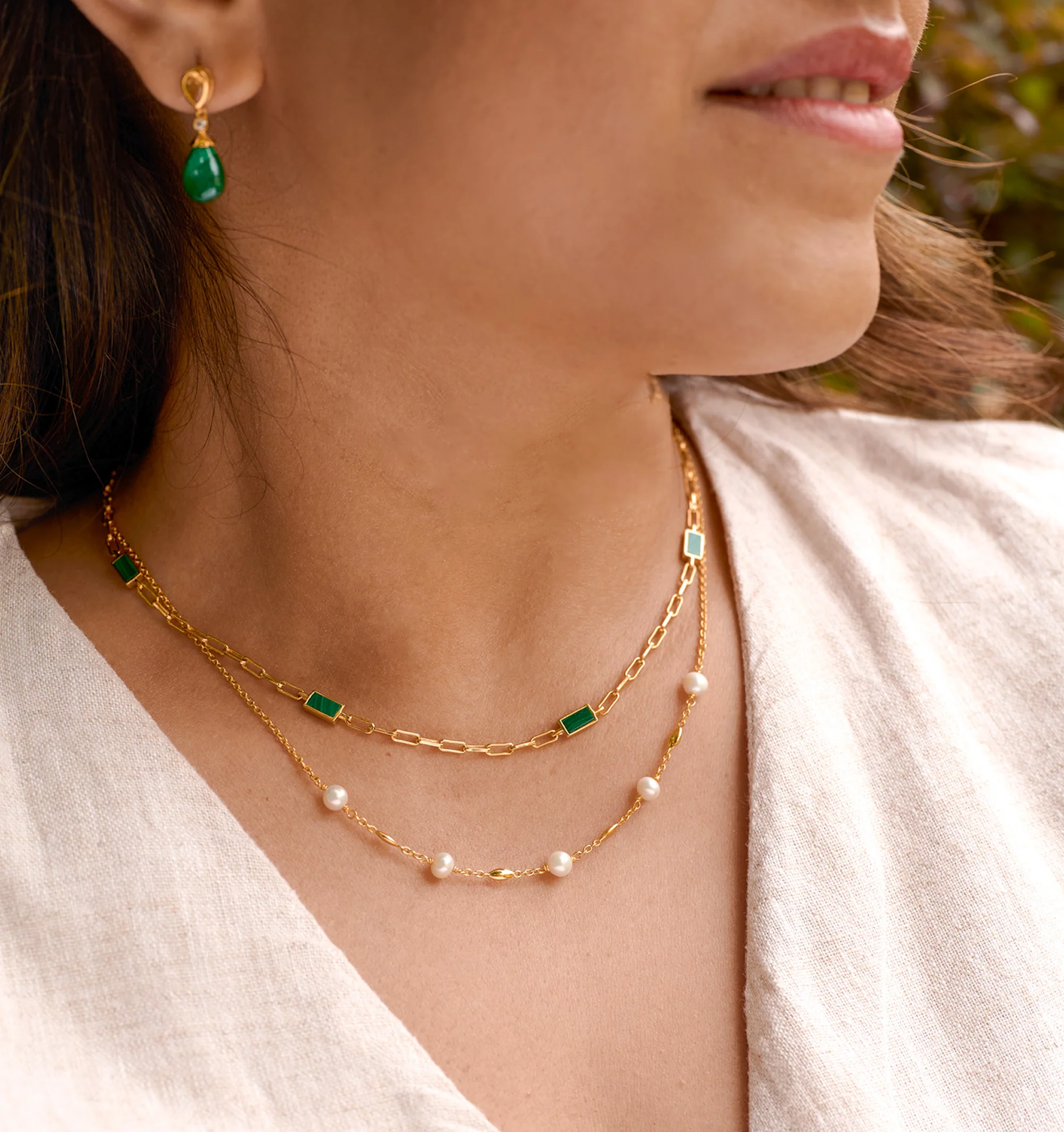 Close-up of a woman wearing the Tarang Necklace with seven malachite stones and pearls on a gold chain, paired with matching green stone earrings.