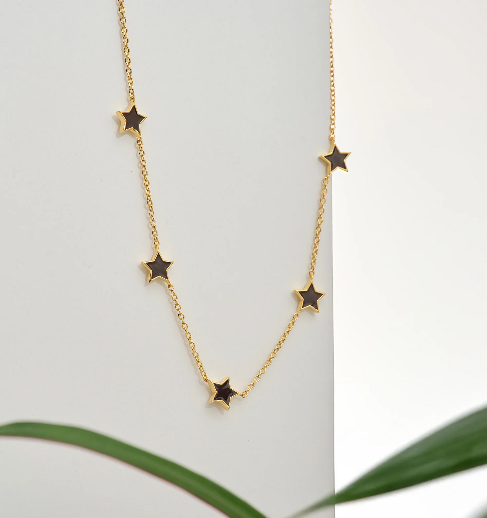 Noctra Necklace gold chain with black star charms on white background