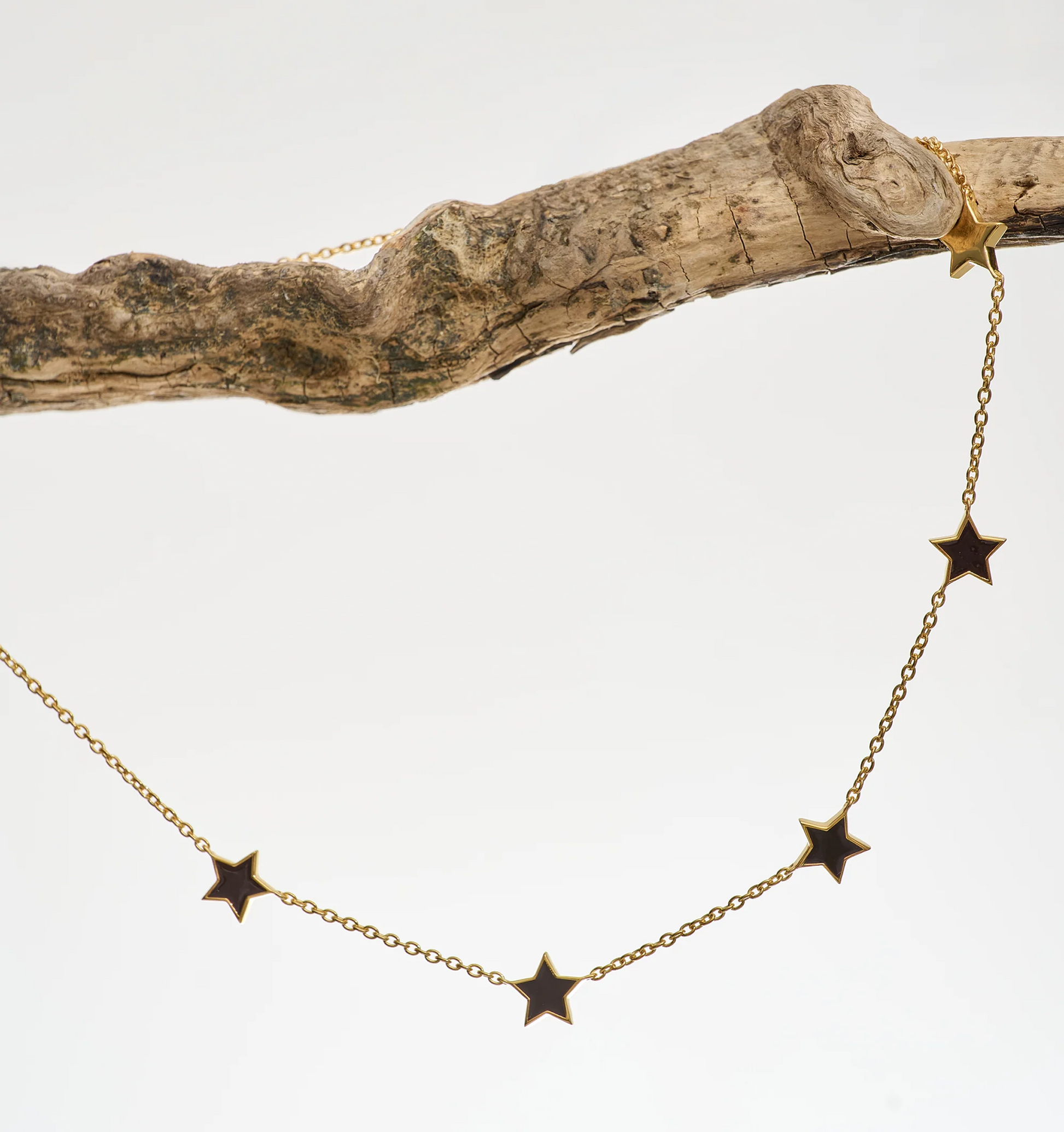 Noctra Necklace gold chain with star-shaped pendants hanging on a rustic branch
