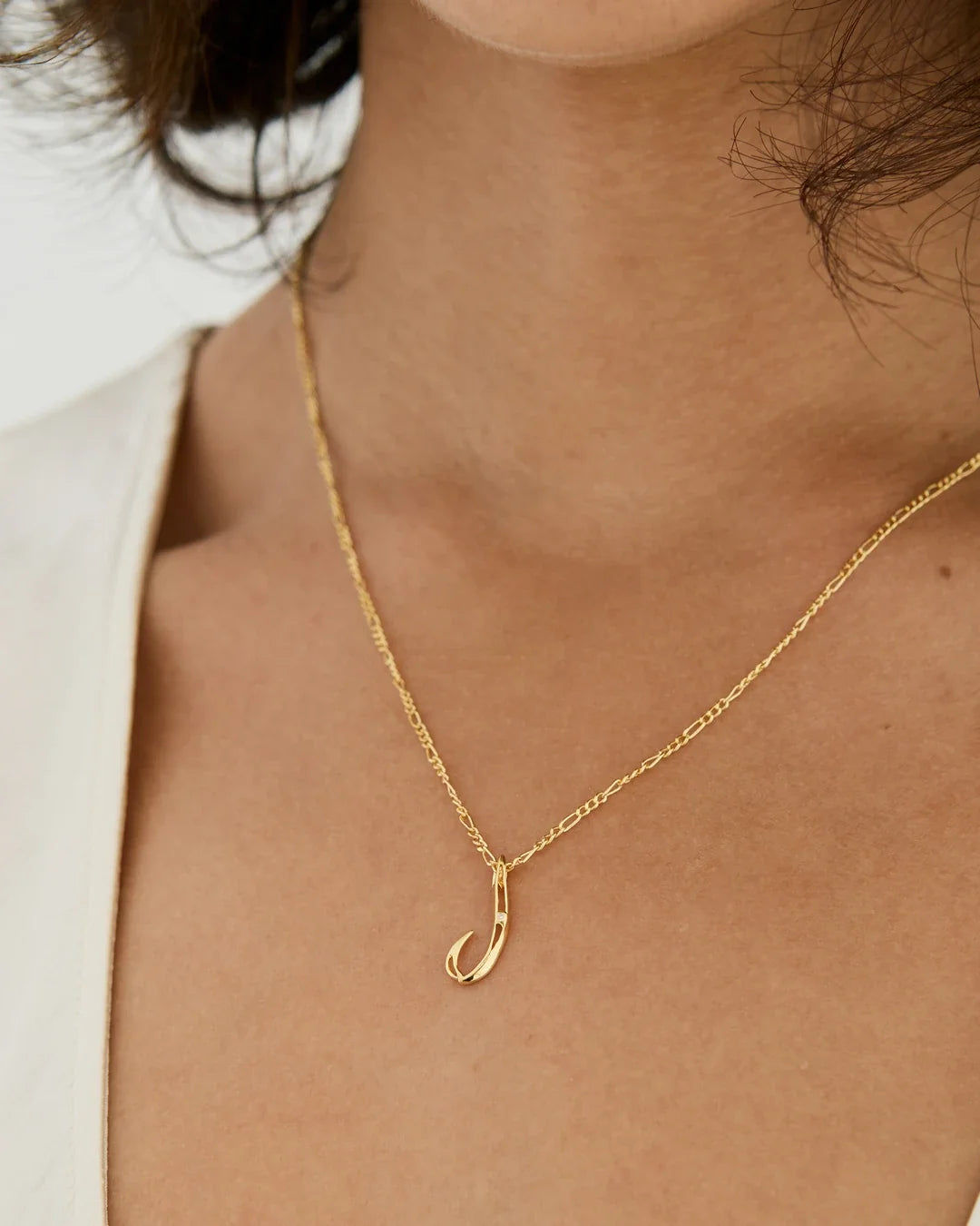 J जे Initial Necklace in gold-tone metal, with a delicate fine-link chain and a small curved J-shaped pendant.