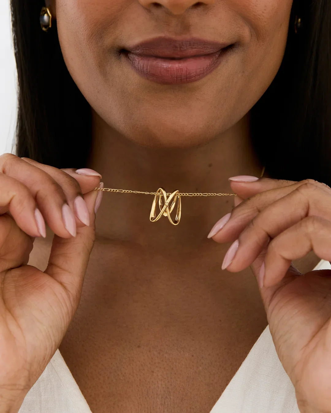 M एम Initial Necklace, a delicate gold-tone chain featuring a sculptural looping M initial pendant held between fingers.
