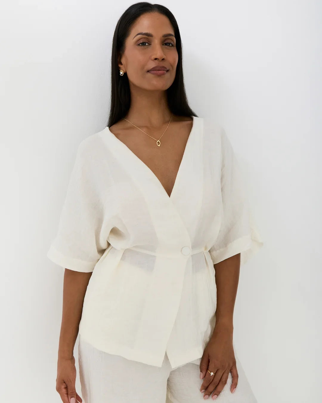O ओ Initial Necklace, fine gold-tone chain with a small oval pendant, worn with a white wrap blouse.