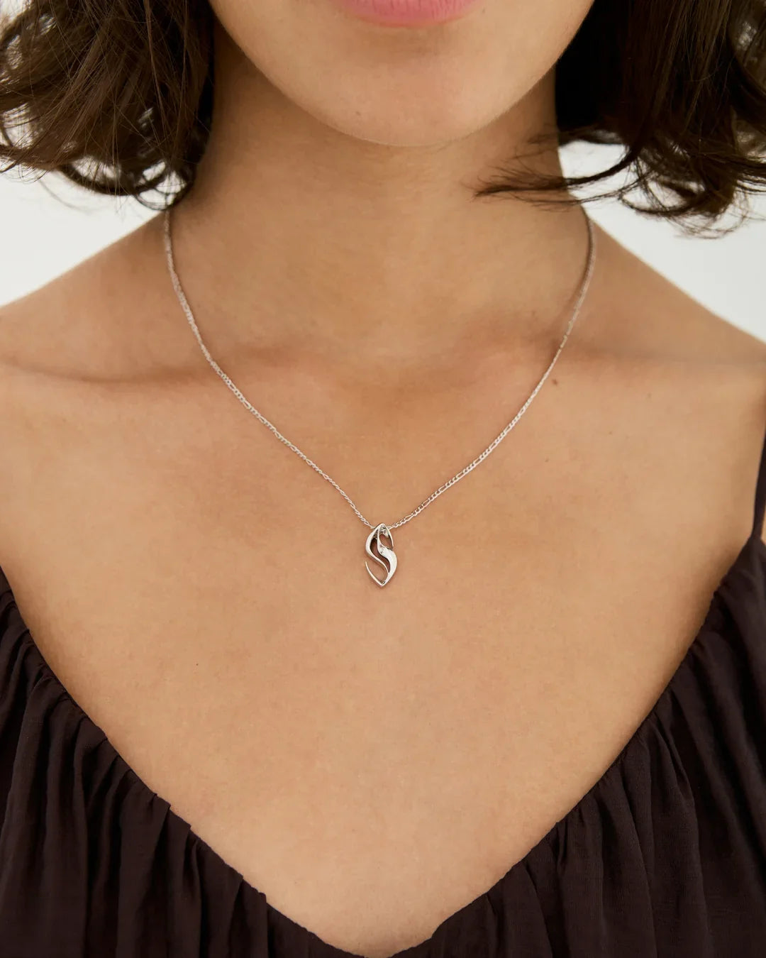S एस Initial Necklace in polished silver, with a delicate chain and a sculptural S-shaped pendant.